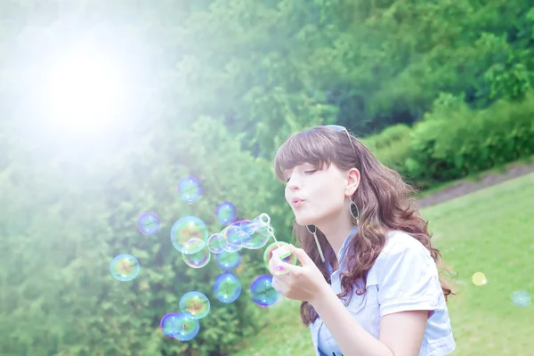 Attractive girl inflating colorful soap bubbles in spring park — Stock Photo, Image