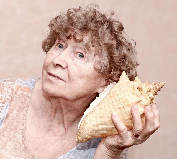 Leende farmor som lyssnar på en snäcka — Stockfoto