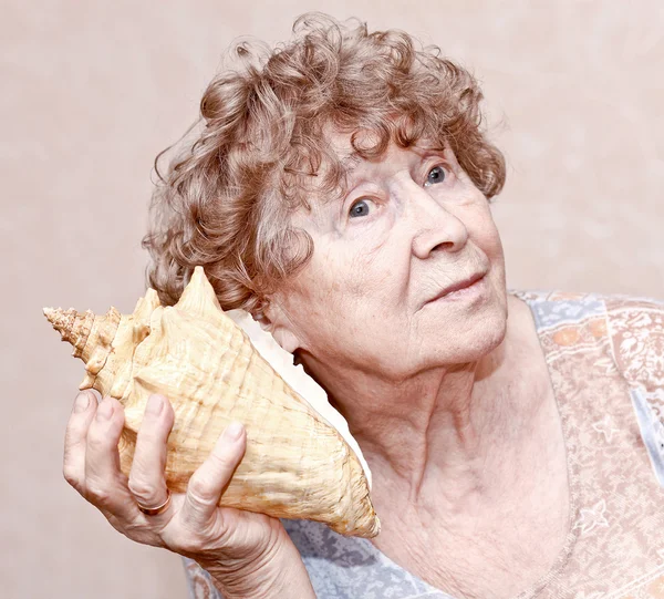 Souriant arrière grand-mère écouter un coquillage — Photo