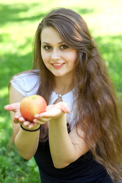 Brunette young girl with an apple in summer park enjoying — Stock Photo, Image