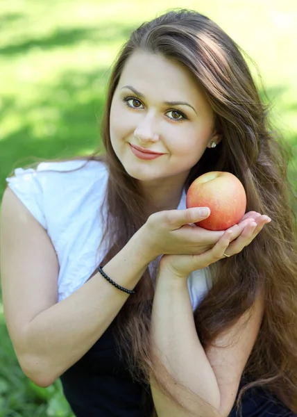 Brünette junge Mädchen mit einem Apfel im Sommerpark genießen — Stockfoto