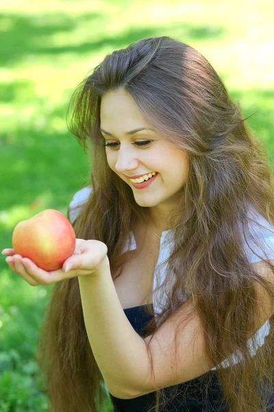 Brunette young girl with an apple in summer park enjoying — Stock Photo, Image