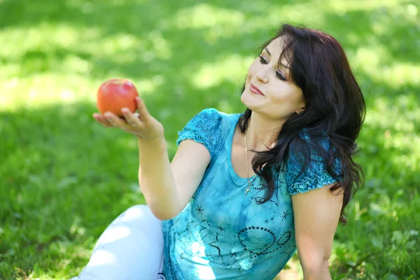 Brunette jonge meisje met een appel in de zomer park genieten van — Stockfoto