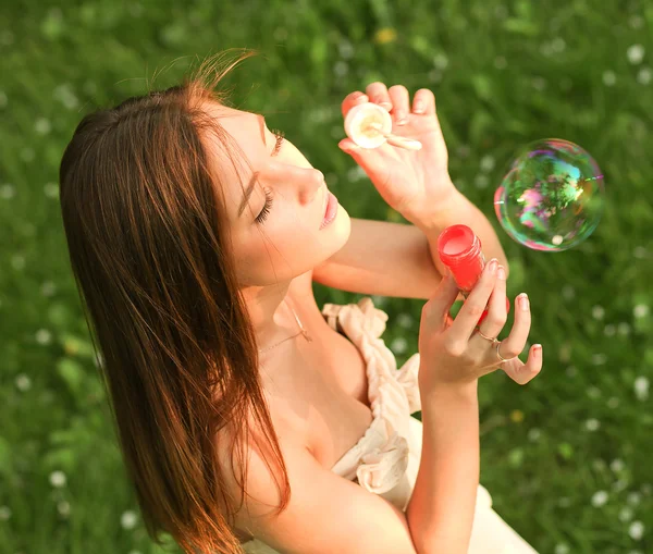 Молодая девушка надувает мыльные пузыри в летнем зеленом парке — стоковое фото
