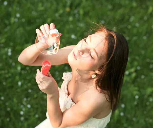 Молодая девушка надувает мыльные пузыри в летнем зеленом парке — стоковое фото