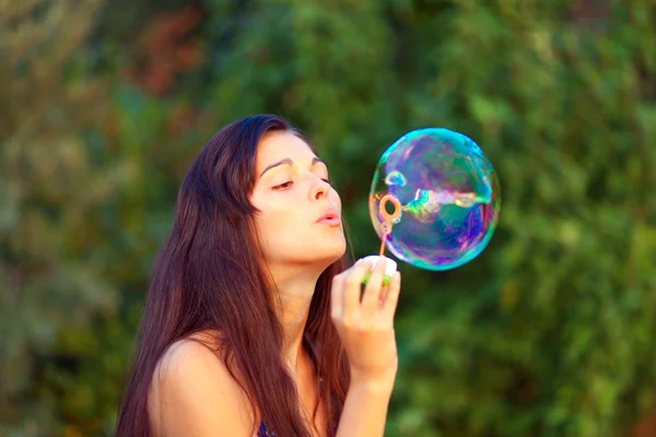 Portret atrakcyjnej młodej dziewczyny nadmuchiwanie kolorowe bańki mydlane zewnątrz — Zdjęcie stockowe