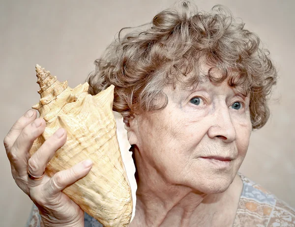 Улыбающаяся прабабушка слушает ракушку — стоковое фото