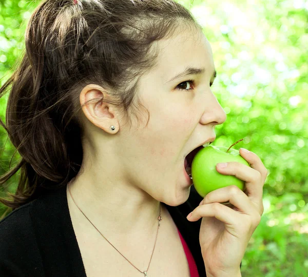 Brunette young girl eating apple in summer park — Stock Photo, Image