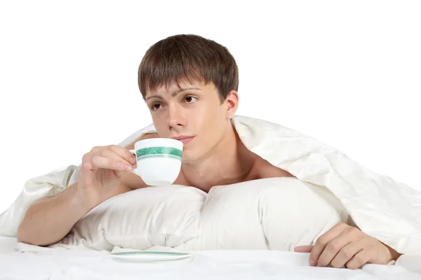 Genç, yatakta yatan ve bir bardak tutan adam — Stok fotoğraf