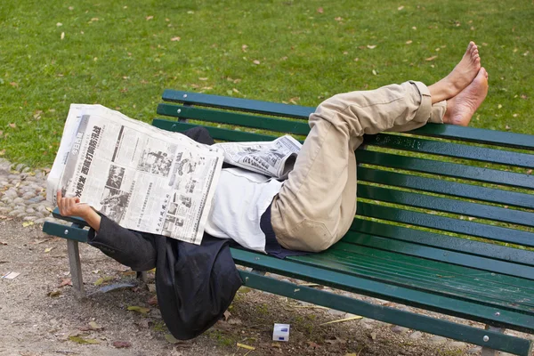 Reads a newspaper lying on a bench — Stock Photo, Image