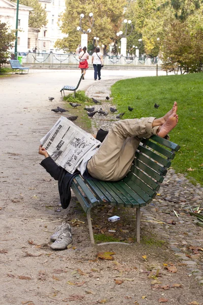 Čte noviny, ležící na lavičce — Stock fotografie