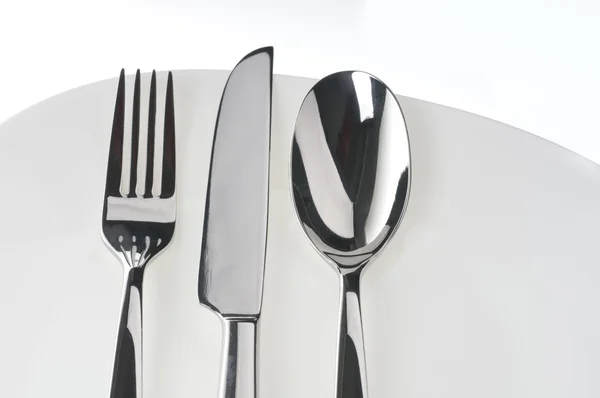 Вилка, ложка и нож на тарелке над белым — стоковое фото