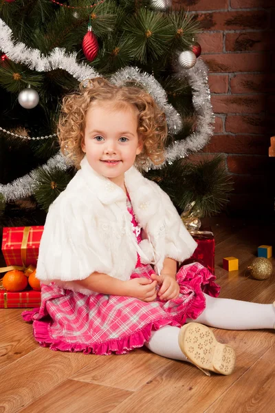Liten flicka sitter nära julgran — Stockfoto
