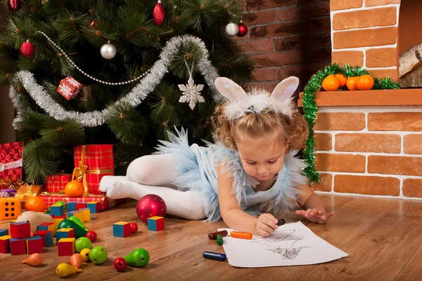 Klein meisje tekening in de buurt van de kerstboom — Stockfoto