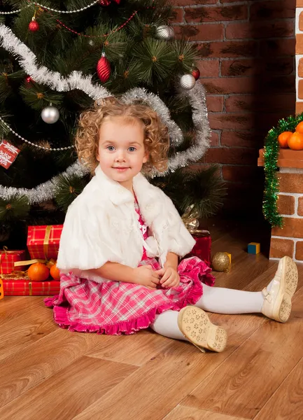 Klein meisje zitten in de buurt van de kerstboom — Stockfoto