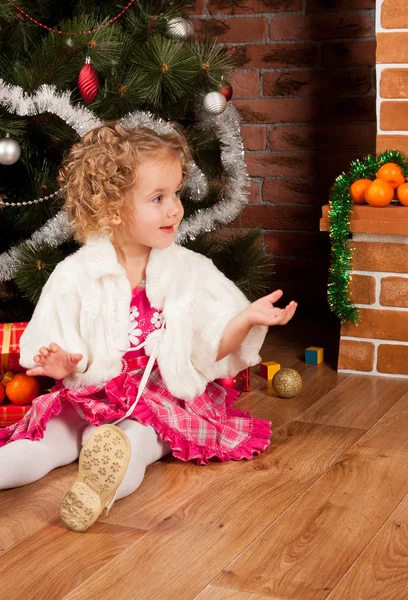 Kleines Mädchen sitzt in der Nähe des Weihnachtsbaums — Stockfoto