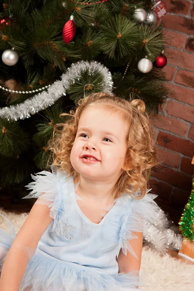 Malá dívka sedí u vánočního stromu — Stock fotografie