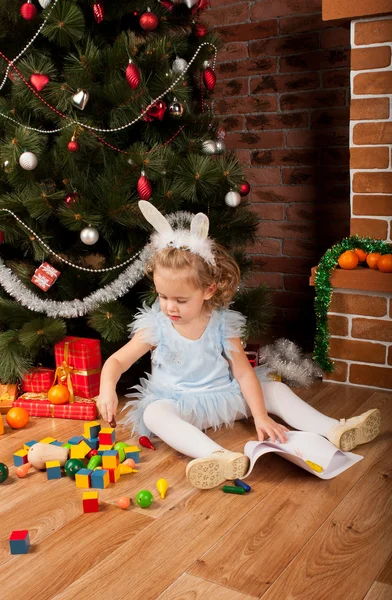 Kleines Mädchen sitzt in der Nähe des Weihnachtsbaums — Stockfoto
