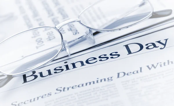 stock image Eyeglasses lie on the newspaper with title Business day. Blue to