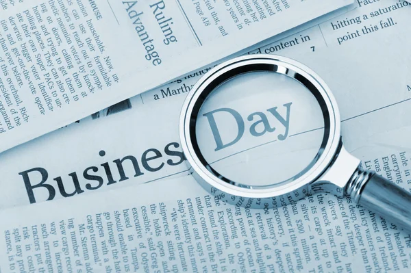 stock image Loupe lies on the newspaper with title Business day. Blue toned