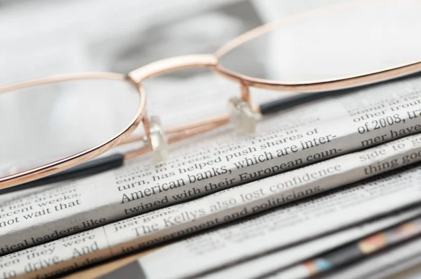 Brýle ležet na hromadu novin — Stock fotografie