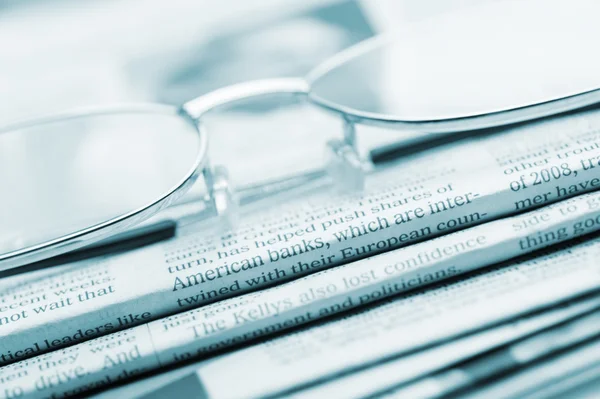 Eyeglasses lie on a pile of newspapers.Blue toned — Stock Photo, Image