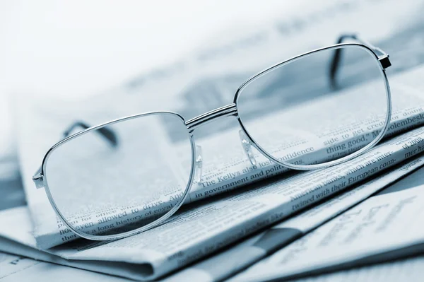 Las gafas de vista se encuentran en una pila de periódicos. Azul tonificado —  Fotos de Stock