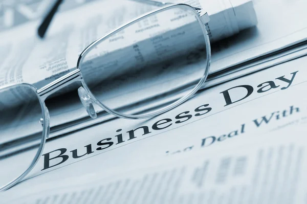 Gli occhiali si trovano sul giornale con il titolo Business day. Blu a — Foto Stock