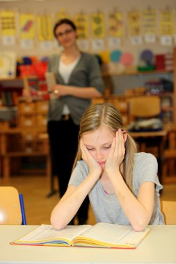 Stressed-out student in the school with a book in front of. clipart