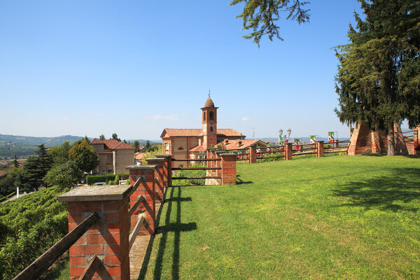 View on old church from green lawn surrounded by brick fence in Grinzane Cavour - small town in northern Italy.
