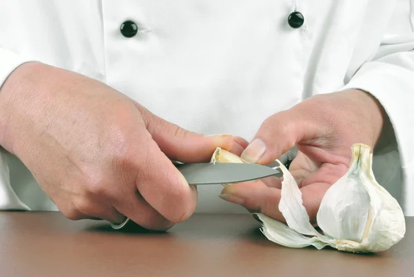 Female chef cuts garlic with a kitchen knife — Stock Photo, Image