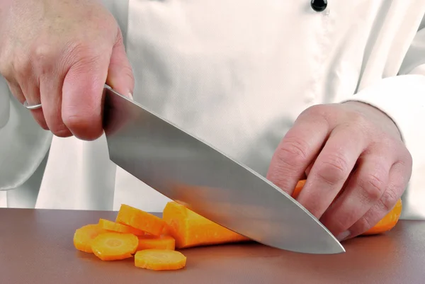 Female chef cuts a carrot with a large kitchen knife — Stock Photo, Image