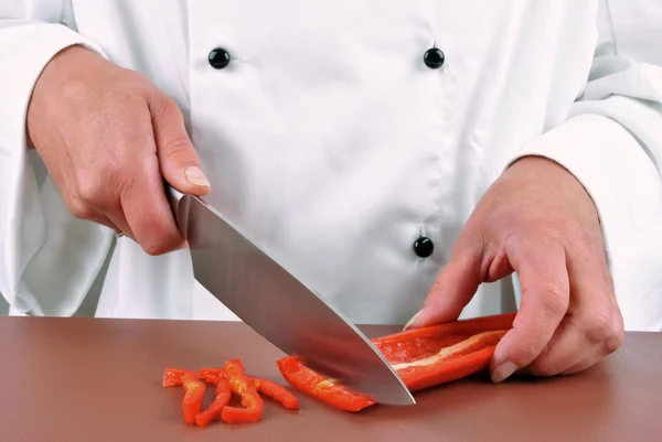 Ženské šéfkuchař připravuje červené papriky s kuchyňským nožem — Stock fotografie