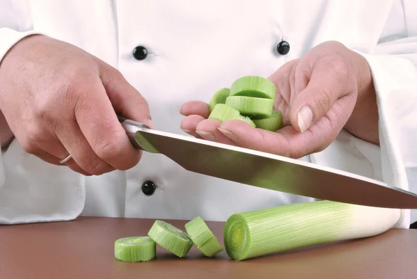 Female chef cuts leek with a large kitchen knife — Stock Photo, Image