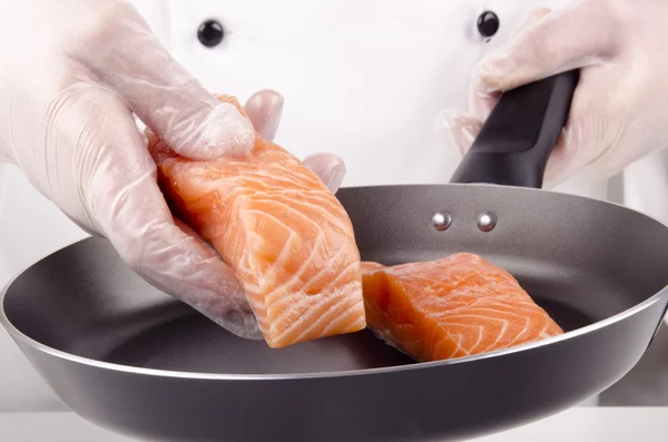 Female chef puts salmon fillets for frying in a pan — Stock Photo, Image