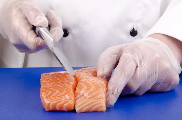 Female chef cuts salmon fillets with a kitchen knife