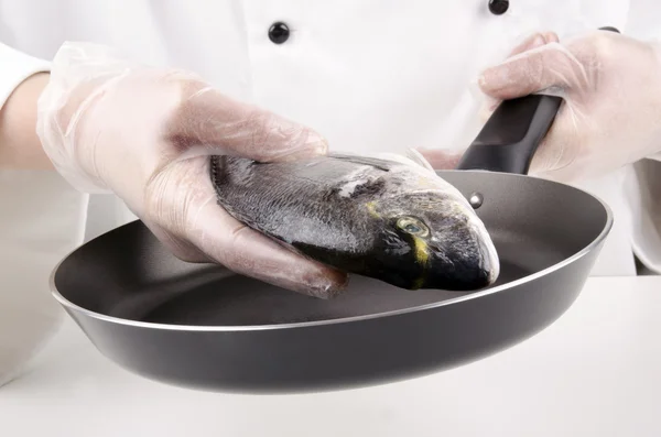 Chef fêmea coloca uma sargo do mar para fritar em uma panela — Fotografia de Stock