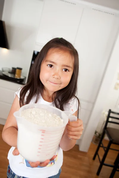Mladá dívka pečení odměrku mouky — Stock fotografie