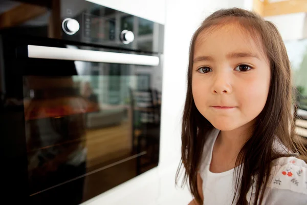 Jong meisje kijken koekjes bakken — Stockfoto
