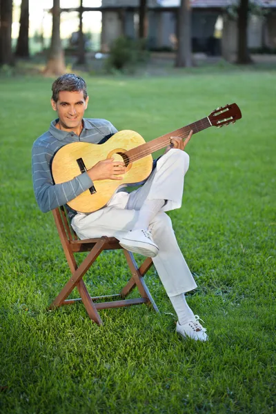 Man spelar gitarr sitter i gräsmatta — Stockfoto