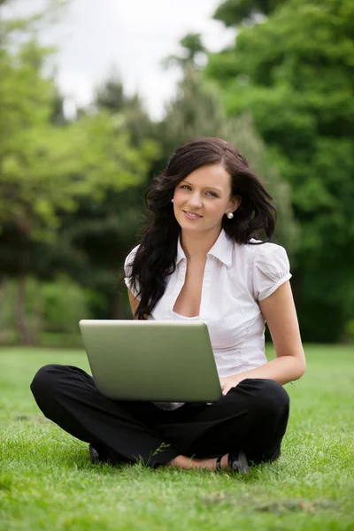 Dizüstü bilgisayar kullanarak çimlerde oturan kadın — Stok fotoğraf
