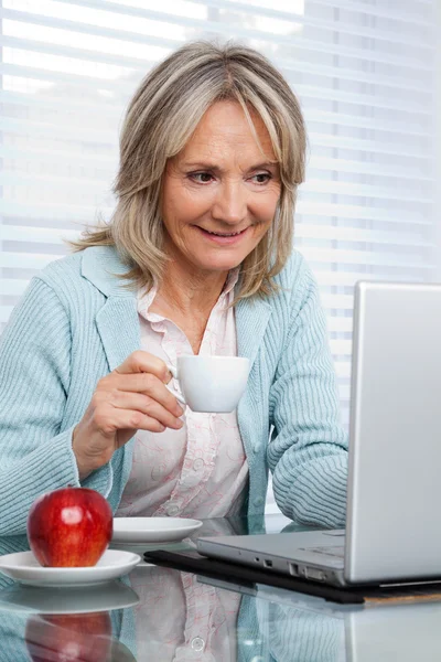 Femme travaillant sur ordinateur portable tout en ayant une tasse de thé — Photo