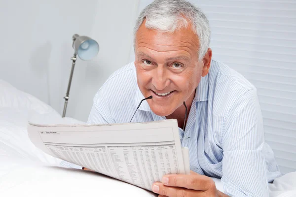 Человек читает газету на кровати — стоковое фото
