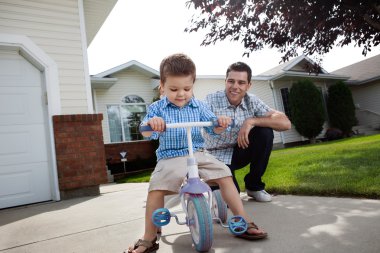 Father teaching Son To Ride a Tricycle clipart