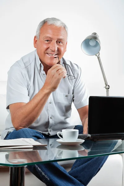 Улыбающийся пожилой человек с ноутбуком на столе — стоковое фото