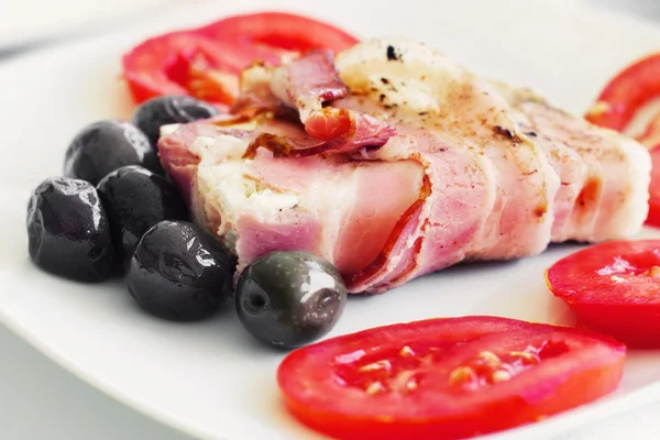 Grilled white cheese wrapped in bacon served with olives and tomatoes — Stock Photo, Image