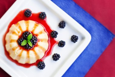 böğürtlen ve nane ile süslenmiş bir tabakta vanilyalı puding