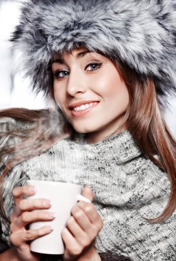 Girl blowing on hot drink dressed in winter clothing clipart