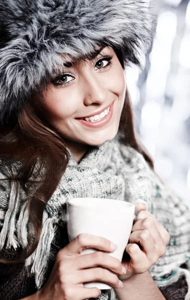 Девушка дует на горячий напиток, одетый в зимнюю одежду — стоковое фото