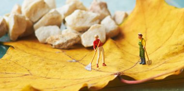 Miniature figurine using a rake to clean up of the fallen leave clipart